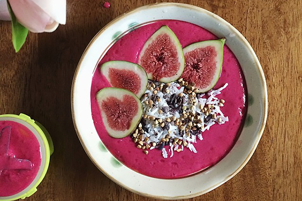 A neon pink smoothie bowl with figs, shredded coconut, organic cacao nibs and pan roasted carob buckwheat granola. From nourishandevolve.